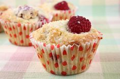 three muffins with raspberries are sitting on a checkered tablecloth