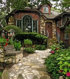 a stone path leading to a house with lots of flowers in the front yard and landscaping around it