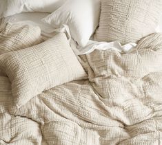 an unmade bed with white pillows and blankets