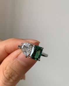 a woman's hand holding an emerald and diamond ring