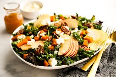 a salad with apples, cheese and pecans in a white bowl on a table