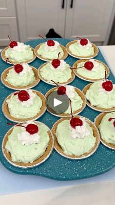 cupcakes with green frosting and cherries are arranged on a blue platter