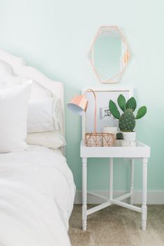 a small white table with a potted plant on it next to a mirror and lamp