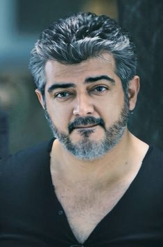 a man with grey hair and beard wearing a black shirt is looking at the camera