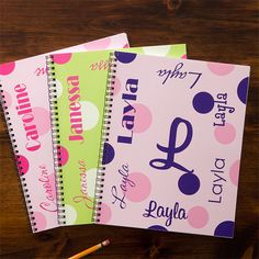 three personalized spiral notebooks on a wooden table with pencils and paper next to them