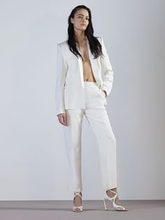 a woman in white suit and heels posing for the camera with her hands on her hips