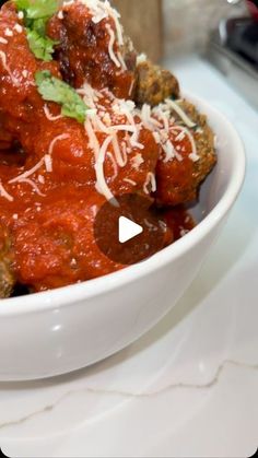 a white bowl filled with meatballs covered in marinara sauce and parmesan cheese