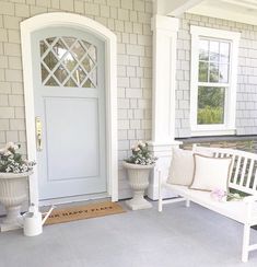 two white benches sitting in front of a door on a porch next to potted flowers