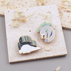 two lapel pins sitting on top of a stone slab next to flowers and petals