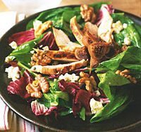 a salad with chicken, lettuce and walnuts in a black bowl on a table