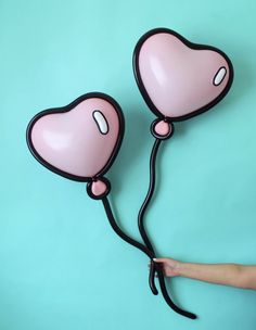 two pink heart shaped balloons being held by someone's hand on a blue background