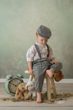 a young boy sitting on top of a stool next to stuffed animals and a clock