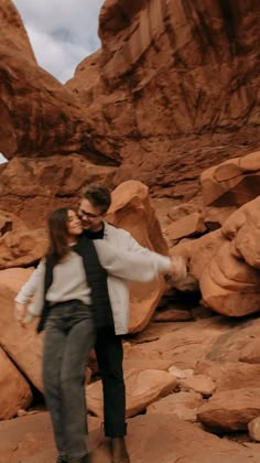 a man and woman standing next to each other in front of large rocks with their arms around each other