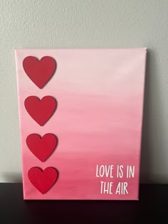 a pink canvas with red hearts and the words love is in the air on it