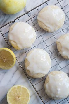 lemon donuts with icing on a cooling rack next to sliced lemons and a lemon wedge