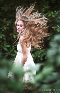 a woman with long hair standing in front of trees