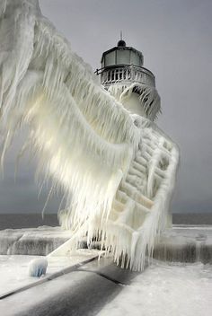 an ice covered lighthouse on the ocean with snow and icicles hanging from it's sides