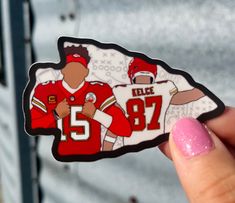 a hand holding up a sticker depicting two football players