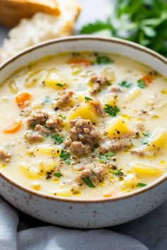 a bowl of soup with meat and cheese in it on a table next to bread