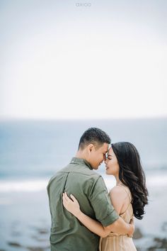 a man and woman standing next to each other in front of the ocean with their arms around each other