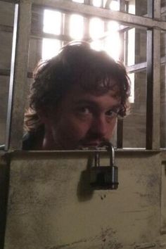 a man is looking through the bars of a jail cell with his face hidden by a padlock