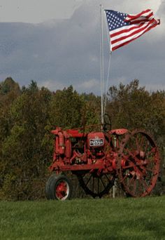 an old red tractor with the american flag on it's side in a field