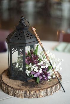 a small black lantern with flowers in it sitting on a piece of wood next to a candle