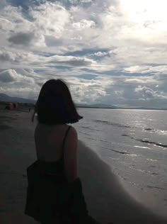 a woman standing on top of a beach next to the ocean under a cloudy sky