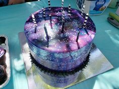 a purple cake with stars on it sitting on top of a table next to cupcakes