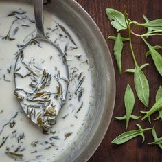 a spoon in a bowl filled with white liquid and green leaves next to it on a wooden table