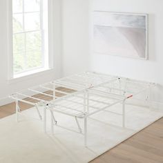 a white bed frame sitting on top of a hard wood floor next to a window