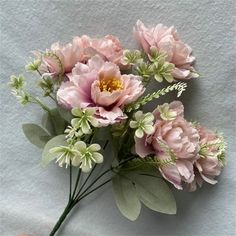 a hand holding a bunch of pink flowers on top of a white wall with green leaves