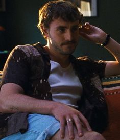 a young man sitting on top of a couch next to a green wall and holding his hand up to his ear