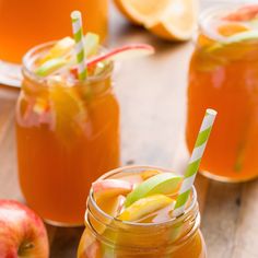 two mason jars filled with apple cider on top of a wooden table next to sliced apples