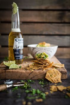 tortilla chips and beer on a cutting board with lime wedges next to it