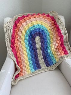 a crocheted rainbow blanket sitting on top of a white chair