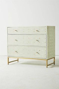 a white and gold chest of drawers with dots on the front, in an empty room