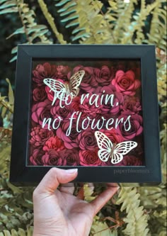 a person holding up a framed sign with flowers and butterflies in the frame that says no rain, no flowers