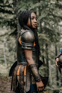 two people dressed in armor standing next to each other on a forest trail with trees behind them