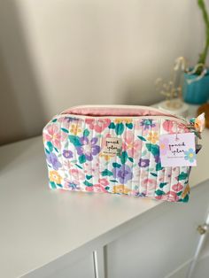 a pink flowered cosmetic bag sitting on top of a white table next to a potted plant