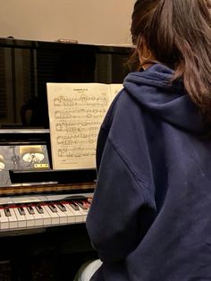 a person sitting in front of a piano with sheet music on the keyboard behind them