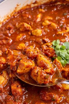 a spoon with some food in it on top of a pan filled with sauce and garnish