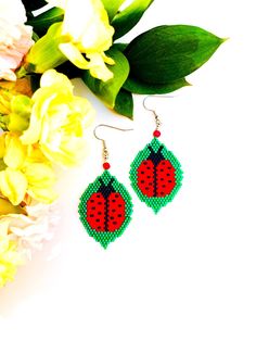 a pair of red and green beaded ladybug earrings next to flowers