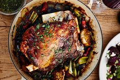 a large pot roast with vegetables and meat in it on a table next to wine glasses