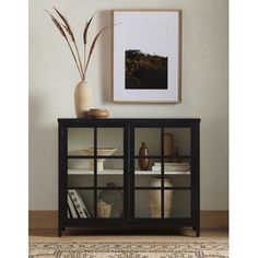 a black cabinet with glass doors on the top and shelves below it, in front of a framed photograph