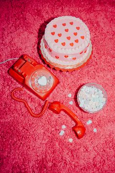 an old fashioned red phone sitting on top of a pink carpet next to a cake