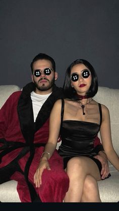 a man and woman sitting on a couch with their eyes covered by blindfolds