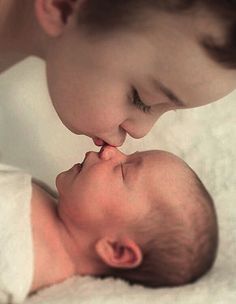 a mother kissing her baby's forehead while laying on top of the other child