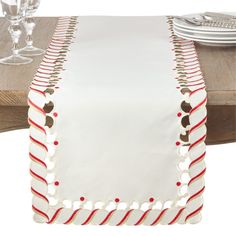 a white table runner with red and gold trimmings on a wooden dining table