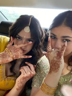 two women with henna on their hands and one holding her hand up to the camera